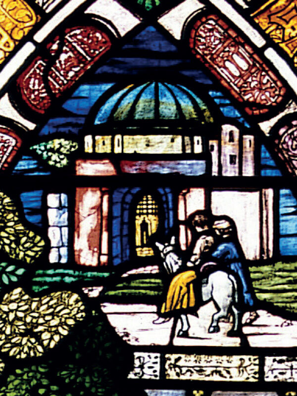 Mary and Joseph travel on a donkey, surrounded by lush greenery and a detailed architectural backdrop in stained glass