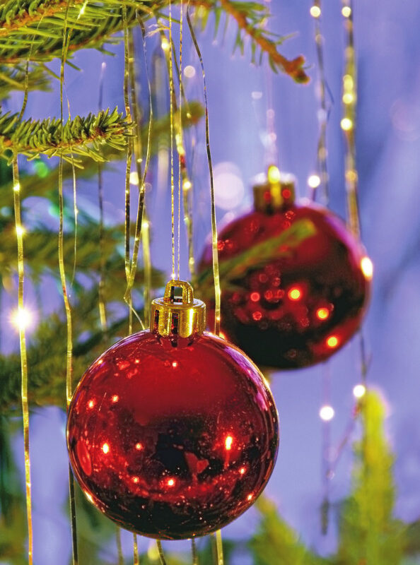 Red Christmas ornaments hang from a tree, surrounded by golden strands and soft, glowing lights in a festive setting