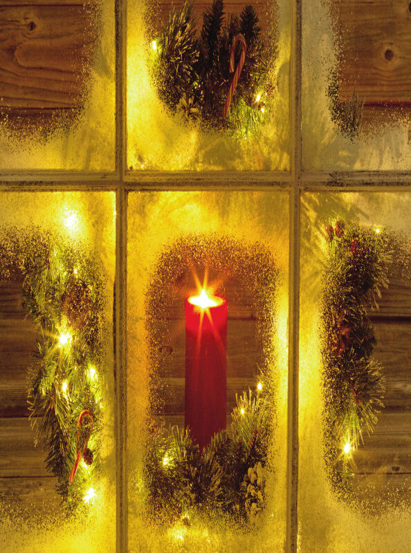 Frosted window with a glowing red candle surrounded by festive greenery and twinkling lights, evoking a cozy Christmas scene