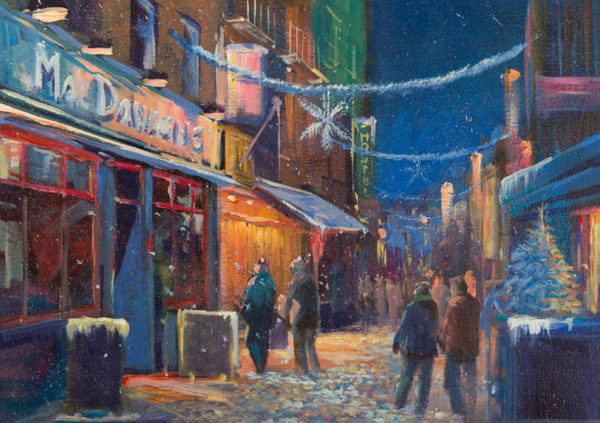 Snow-covered Quay Street in Galway, illuminated by festive lights and bustling with people during the Christmas season
