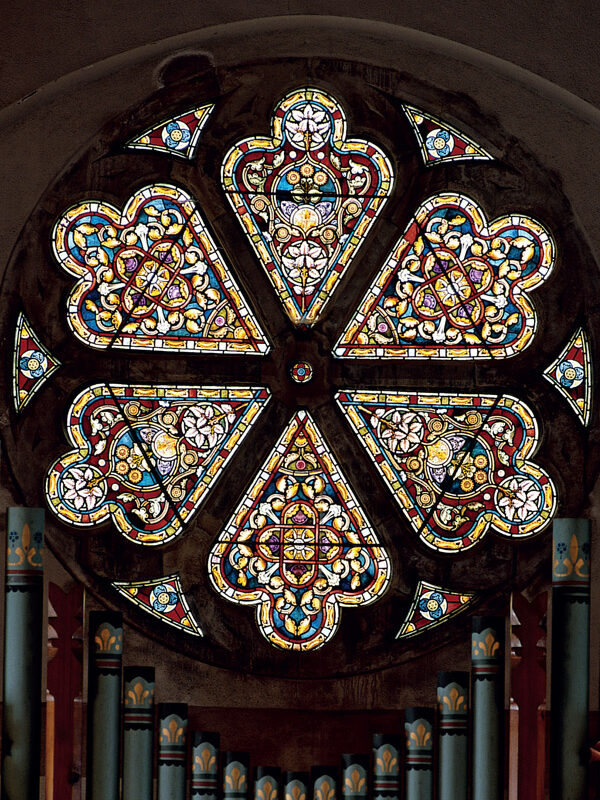 Stained glass rose window featuring intricate floral patterns and vibrant colors, set against a dark background