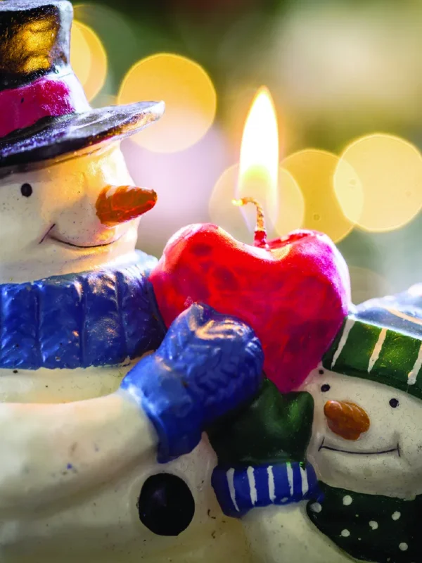 Two cheerful snowmen hold a red heart candle, glowing warmly against a blurred festive background. Snowmen and the Red Candle